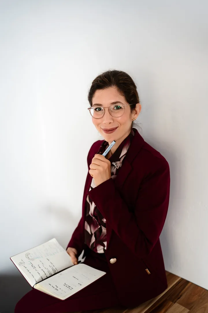 Livits Réka bordó kabátban ül, ölében nyitott füzet, kezében toll.